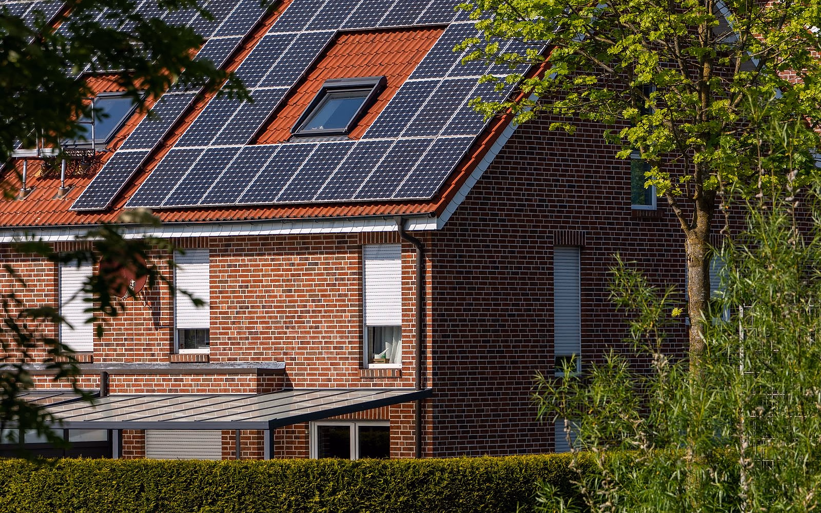 A brick home with rooftop solar panels among mature trees